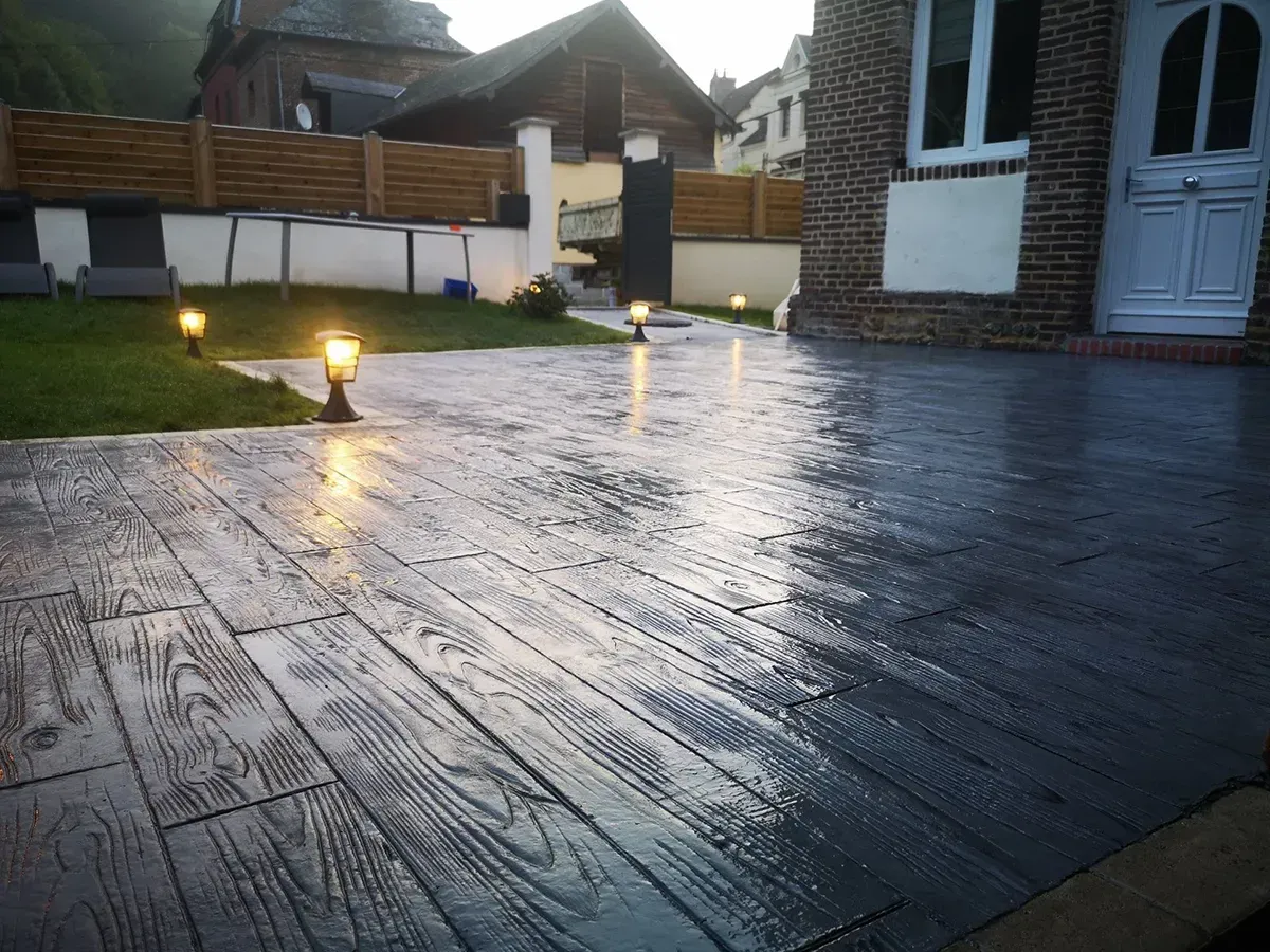 Terrasse en béton imprimé effet bois anthracite éclairée en soirée en Seine-Maritime